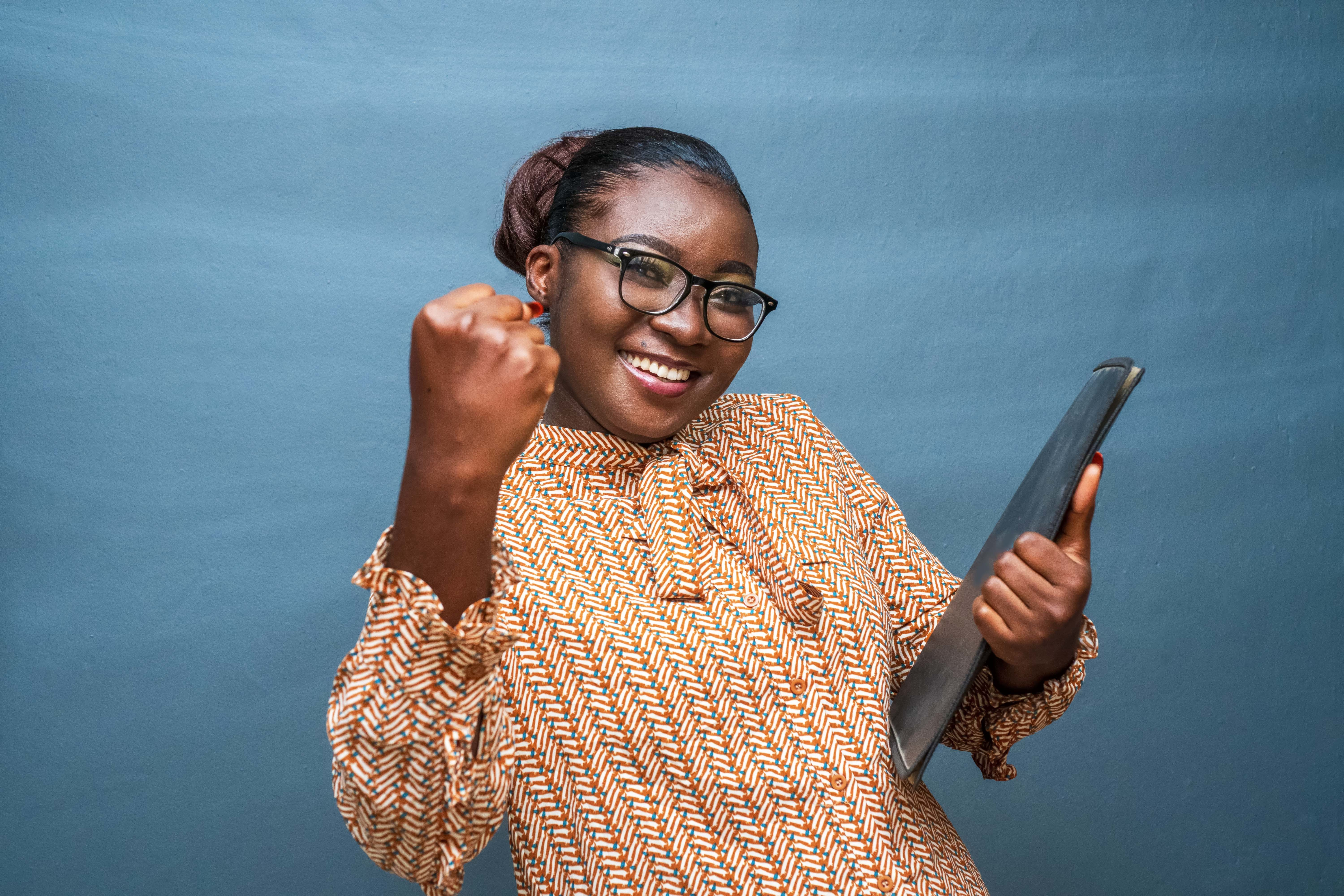 Smiling professional with a raised fist, holding a laptop, against a blue wall
